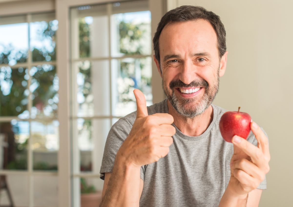 Smiling middle-aged man after teeth replacement with dental implants eating an apple.